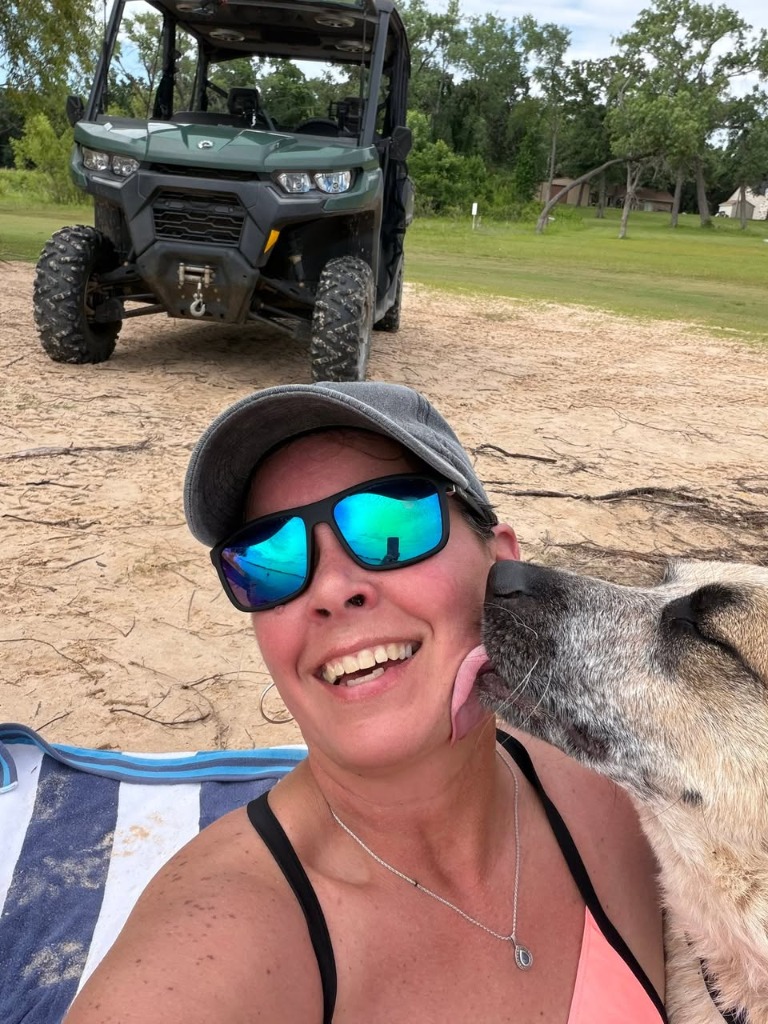 Tammy on the sandy beach of Lake Texoma with their dog and their side-by-side vehicle in the background.